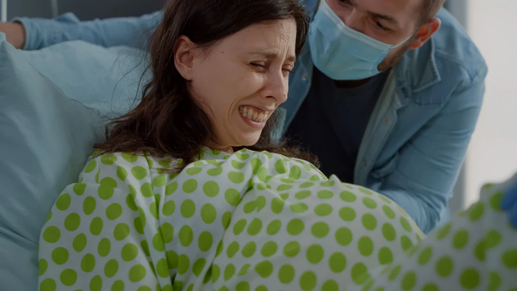 close up pregnant woman pain delivering child hospital ward bed caucasian man helping wife with labor contractions giving assistance couple childbirth preparing parenthood